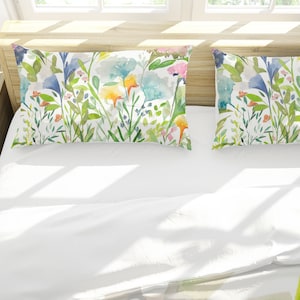 May include: Two white pillowcases with a floral pattern. The pattern features watercolor-style flowers in shades of blue, green, yellow, and pink on a white background.