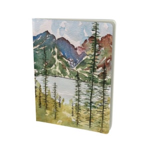 May include: Watercolor painting of a mountain landscape with a lake in the foreground. The mountains are painted in shades of blue, green, and purple, and the lake is a light blue. There are trees in the foreground, painted in shades of green and brown.