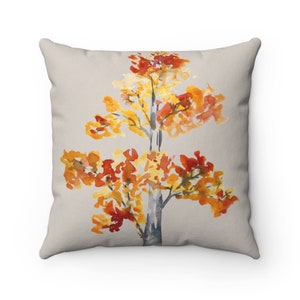May include: A throw pillow with a watercolor design of a tree with orange, yellow, and red leaves on a light gray background.
