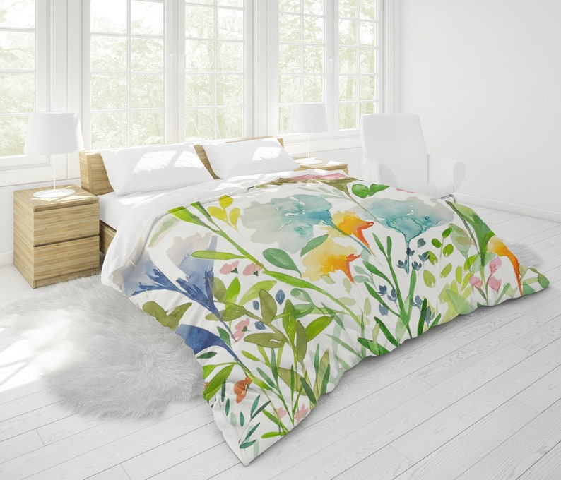 May include: A white duvet cover with a watercolor floral print featuring blue, green, yellow, and orange flowers and leaves.