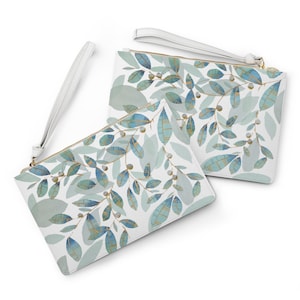 May include: Two white clutch bags with a botanical leaf pattern in shades of blue and gold. Each bag has a white wrist strap and a gold zipper. The leaves are arranged in a repeating pattern across the surface of the bags.
