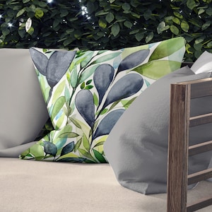 May include: A throw pillow with a watercolor design of blue and green leaves on a white background.