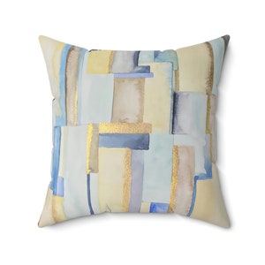 Op de afbeelding: Een decoratief kussen met een geometrisch patroon in tinten blauw, geel en bruin. Het patroon bevat abstracte vormen en gouden accenten.