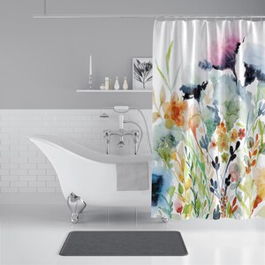 May include: A white bathtub with a gray towel hanging over the side. A shower curtain with a watercolor floral design hangs behind the tub. The shower curtain features a variety of colors, including blue, green, yellow, orange, and pink.