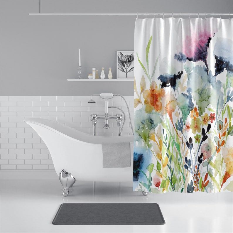 May include: A white bathtub with a gray towel hanging over the side. A shower curtain with a watercolor floral design hangs behind the tub. The shower curtain features a variety of colors, including blue, green, yellow, orange, and pink.