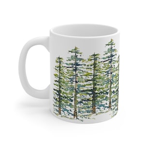 May include: White ceramic mug featuring a watercolor painting of a forest of tall green trees. The trees have dark brown trunks and light green and dark green foliage. The mug has a white handle.