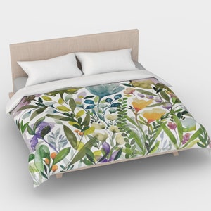 K&ouml;nnte beinhalten: Ein wei&szlig;er Bettbezug mit einem Blumenmuster aus gr&uuml;nen Bl&auml;ttern, gelben, violetten und blauen Blumen. Der Bettbezug liegt auf einem Bett mit einem Holz-Kopfteil.