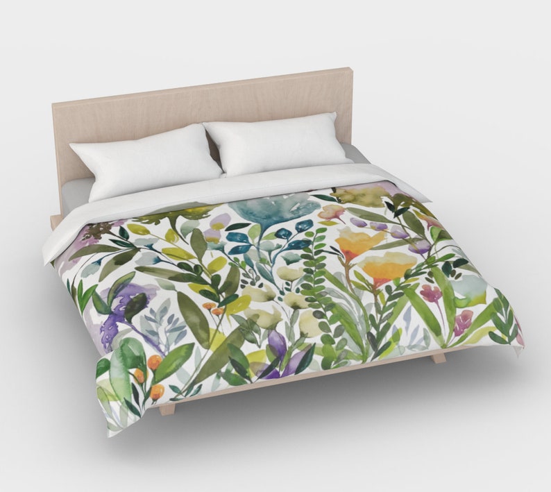 K&ouml;nnte beinhalten: Ein wei&szlig;er Bettbezug mit einem Blumenmuster aus gr&uuml;nen Bl&auml;ttern, gelben, violetten und blauen Blumen. Der Bettbezug liegt auf einem Bett mit einem Holz-Kopfteil.