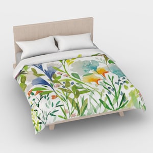 May include: A white duvet cover with a watercolor floral print featuring blue, yellow, green, and orange flowers. The duvet cover is on a bed with a wooden headboard and two white pillows.