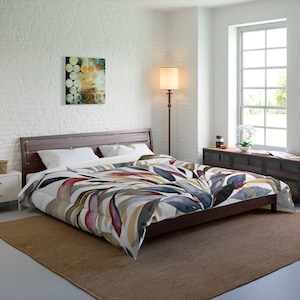 May include: A bed with a white duvet cover featuring a watercolor design of abstract leaves in shades of blue, red, yellow, and brown. The bed has a wooden headboard and is sitting on a rug.
