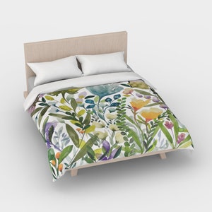 K&ouml;nnte beinhalten: Ein wei&szlig;er Bettbezug mit einem Blumenmuster aus gr&uuml;nen Bl&auml;ttern, gelben, orangefarbenen und violetten Bl&uuml;ten.
