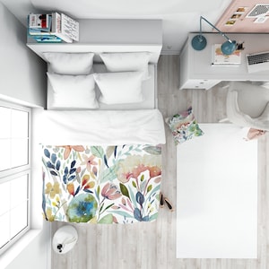 May include: A white bed with a floral duvet cover featuring watercolor flowers in shades of pink, blue, yellow, and green. The bed has two white pillows and a white throw pillow with a floral pattern.