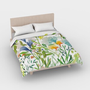 May include: A white duvet cover with a watercolor floral print featuring blue, yellow, green, and orange flowers. The duvet cover is on a bed with a wooden headboard.