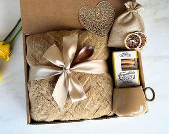 May include: A gift box filled with a brown throw blanket, a wooden spoon, a small bag of cookies, and a brown mug. The box is decorated with a heart-shaped cutout and a small bag of lemons.