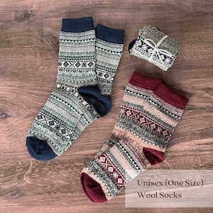 Puede incluir: Dos pares de calcetines de lana con dise&ntilde;os estampados en azul marino, verde, blanco y burdeos. Un par est&aacute; doblado y atado con una cuerda blanca. El texto "Unisex (One Size) Wool Socks" es visible.