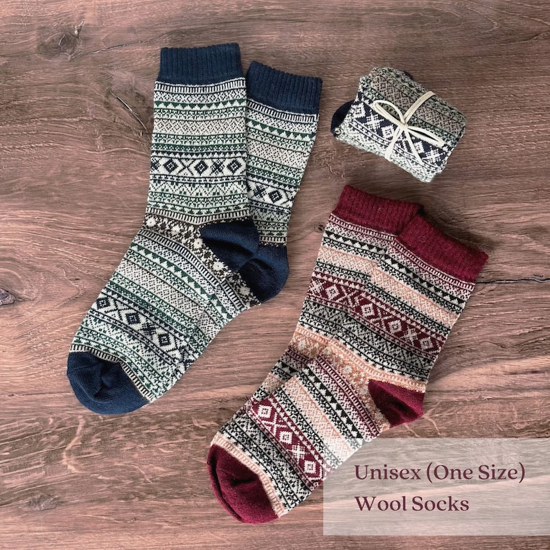 Puede incluir: Dos pares de calcetines de lana con dise&ntilde;os estampados en azul marino, verde, blanco y burdeos. Un par est&aacute; doblado y atado con una cuerda blanca. El texto "Unisex (One Size) Wool Socks" es visible.