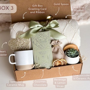 Peut inclure: Une bo&icirc;te-cadeau en carton brun remplie de divers articles, dont une couverture blanche, une tasse en c&eacute;ramique mouchet&eacute;e, une tablette de chocolat gourmet, un dessous-de-verre en forme de c&oelig;ur, une cuill&egrave;re en or, une petite plante succulente en pot et des tranches de citron s&eacute;ch&eacute;es. La bo&icirc;te comprend &eacute;galement une carte de v&oelig;ux et un ruban.