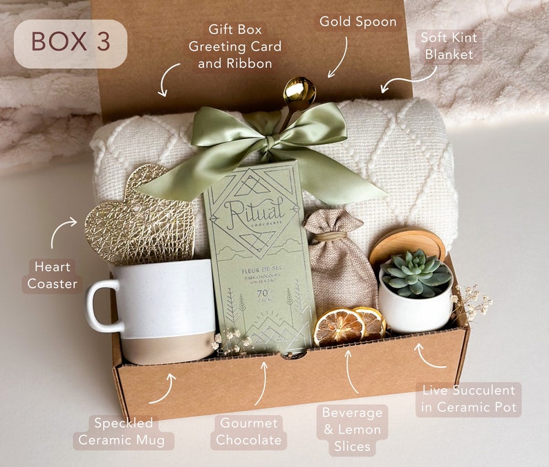 Peut inclure: Une bo&icirc;te-cadeau en carton brun remplie de divers articles, dont une couverture blanche, une tasse en c&eacute;ramique mouchet&eacute;e, une tablette de chocolat gourmet, un dessous-de-verre en forme de c&oelig;ur, une cuill&egrave;re en or, une petite plante succulente en pot et des tranches de citron s&eacute;ch&eacute;es. La bo&icirc;te comprend &eacute;galement une carte de v&oelig;ux et un ruban.