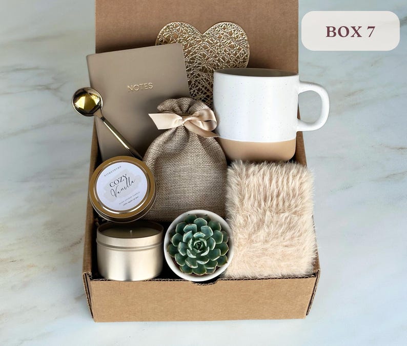 May include: A brown cardboard box with the text "BOX 7" printed on the side. The box contains a variety of items, including a white mug with a brown bottom, a small potted succulent, a candle, a notebook, a gold spoon, and a small burlap bag.