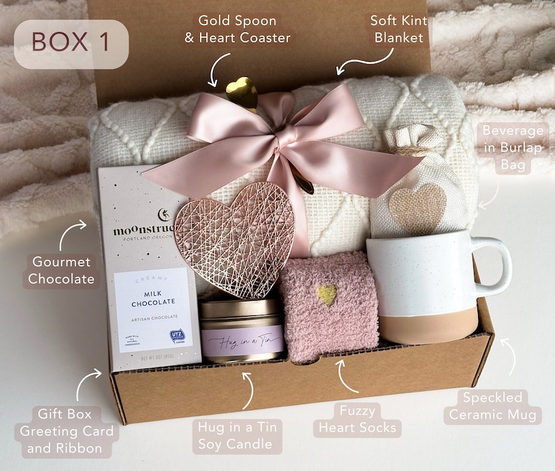 Peut inclure: Une bo&icirc;te-cadeau remplie d'articles de soins personnels, comprenant une couverture en tricot blanc doux, une chaussette en forme de c&oelig;ur rose et moelleuse, une tasse en c&eacute;ramique mouchet&eacute;e, une barre de chocolat gastronomique, une bougie de soja et une boisson dans un sac en toile de jute. La bo&icirc;te est &eacute;tiquet&eacute;e "BOX 1".
