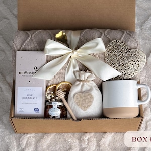 May include: A gift box filled with a cozy blanket, a mug, a bag of milk chocolate, a jar of honey, and a decorative heart. The box is labeled "BOX 6".