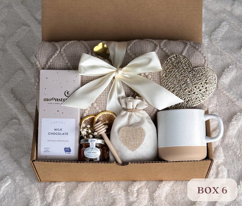 May include: A gift box filled with a cozy blanket, a mug, a bag of milk chocolate, a jar of honey, and a decorative heart. The box is labeled "BOX 6".
