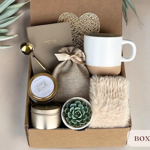 May include: A brown cardboard gift box filled with a variety of items, including a mug, a candle, a small succulent plant, a notebook, a spoon, and a small bag. The box is labeled "BOX 8".