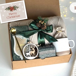 May include: A brown cardboard gift box filled with a cozy blanket, a mug, a small bag, a wooden reindeer ornament, and a card that says "Merry Christmas".