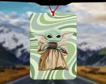 May include: A green and brown car air freshener featuring a cartoon character holding a bowl. The background is a swirling green and white pattern.