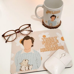 May include: A beige mouse mat with a daisy pattern and the text "Treat People With Kindness". A cartoon illustration of a person with a bird on their shoulder is on the left side of the mouse mat. A white computer mouse is on the right side of the mouse mat.