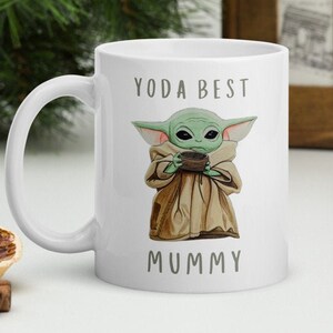 May include: White ceramic mug with a green cartoon character holding a cup. The text "Yoda Best Mummy" is printed on the mug.