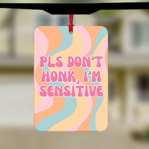 Pode incluir: Um aromatizador de carro com um padrão de espiral colorido e o texto "PLS DON'T HONK, I'M SENSITIVE" em letras cor-de-rosa.