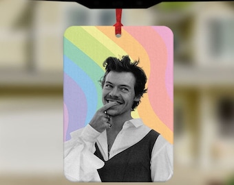 May include: A car air freshener featuring a black and white photo of a person with a rainbow background. The person is smiling and has their finger on their chin.