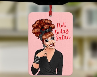 May include: Pink car air freshener with a cartoon image of a woman with red hair and a black dress. The text "Not today Satan" is written in red letters.