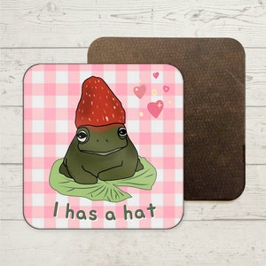 May include: A green frog wearing a red strawberry hat sits on a green leaf. The background is a pink and white gingham pattern. The text "I has a hat" is written below the frog.