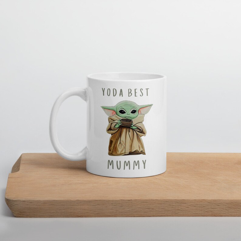 May include: White ceramic mug with a green and brown cartoon character holding a cup. The text "YODA BEST MUMMY" is printed on the mug.