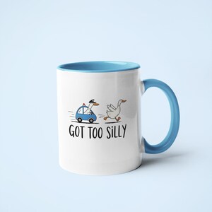 May include: White ceramic mug with a blue interior and handle. The mug features a cartoon illustration of a goose being chased by a police car, with the text "GOT TOO SILLY".
