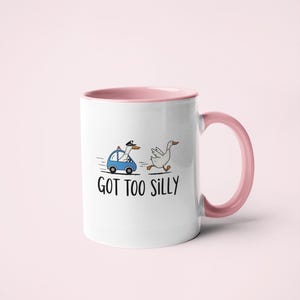 May include: White ceramic mug with a pink interior and handle. The mug features a cartoon illustration of a goose being chased by a police car, with the text "GOT TOO SILLY" below the illustration.