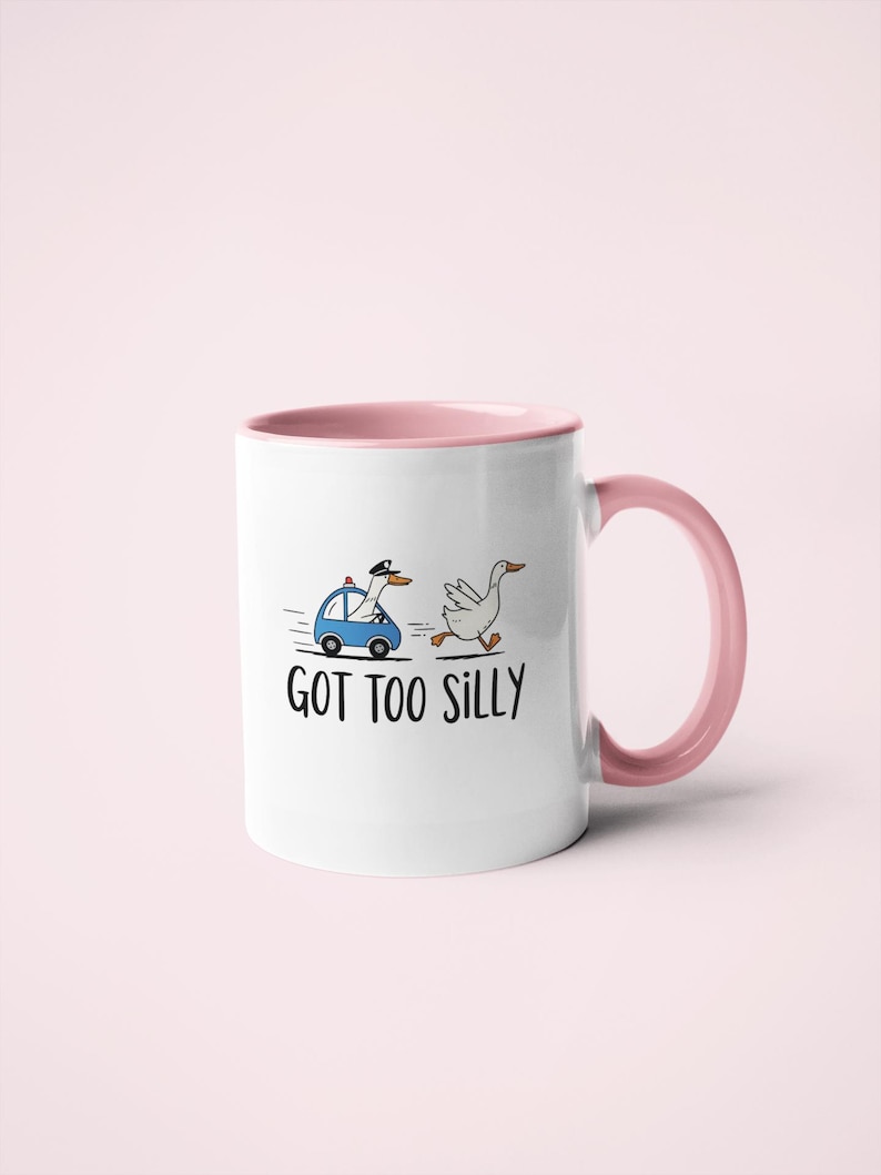 May include: White ceramic mug with a pink interior and handle. The mug features a cartoon illustration of a goose being chased by a police car, with the text "GOT TOO SILLY" below the illustration.