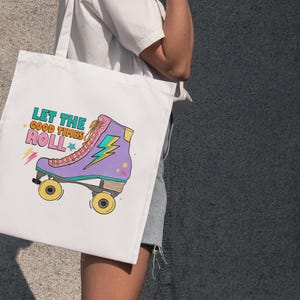 May include: White tote bag with a colourful illustration of a roller skate and the text "Let the good times roll." The roller skate is purple, pink, and yellow with a lightning bolt design. The bag is held by a person.