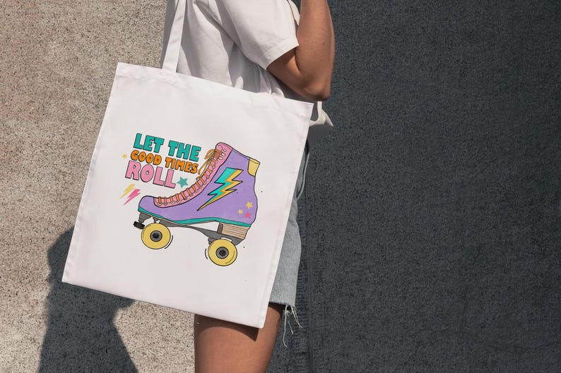 May include: White tote bag with a colourful illustration of a roller skate and the text "Let the good times roll." The roller skate is purple, pink, and yellow with a lightning bolt design. The bag is held by a person.