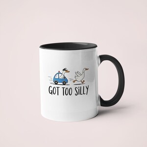 May include: White ceramic mug with a black interior and handle. The mug features a cartoon illustration of a goose being chased by a police car, with the text "GOT TOO SILLY" below the illustration.