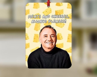 May include: Rectangular ornament with a smiling man in a black turtleneck, surrounded by cheese illustrations. The text "MEATS AND CHEESES, ALWAYS PLEASES!" is displayed in black font on a yellow background. A red ribbon is attached for hanging.