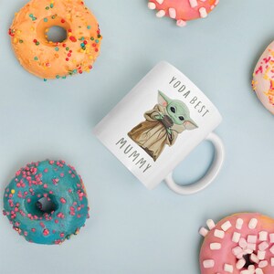 May include: White ceramic mug with a green cartoon character holding a cup. The mug has the text "Yoda Best Mummy" printed on it.