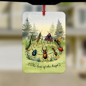 May include: A rectangular hanging air freshener featuring a whimsical illustration of various insects holding hands in a circle on a grassy field. The scene includes a praying mantis, grasshopper, moth, bee, ladybug, ant, and beetle under a crescent moon.