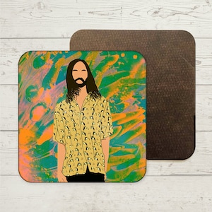 May include: A square coaster featuring a colourful abstract background. The background is a mix of green, blue, orange, and pink. A person with long brown hair and a beard is wearing a yellow shirt with a pattern of small white faces. The person is standing in front of the colourful background.