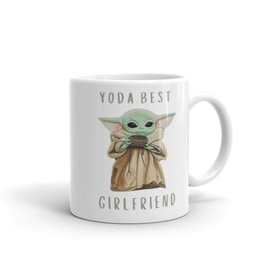 Op de afbeelding: Een witte keramische mok met een groen cartoonfiguur dat een kopje vasthoudt. De tekst "YODA BEST GIRLFRIEND" staat op de mok gedrukt.