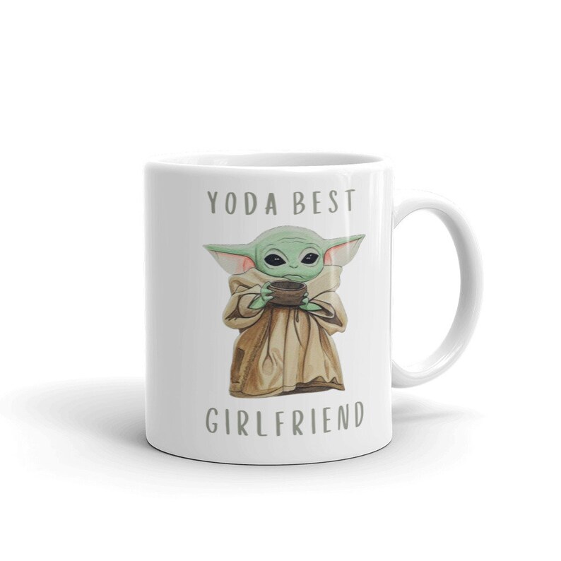 Op de afbeelding: Een witte keramische mok met een groen cartoonfiguur dat een kopje vasthoudt. De tekst "YODA BEST GIRLFRIEND" staat op de mok gedrukt.