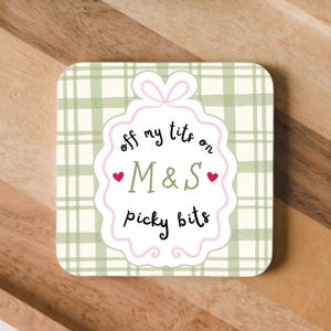 May include: A square coaster with a light green and cream plaid pattern. In the centre, a white scalloped label with a pink outline features the black text "off my tits on M&S picky bits" with two small pink hearts flanking the letters M&S.