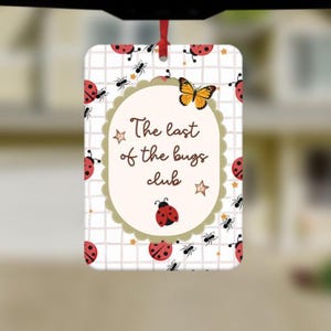 May include: Rectangular air freshener with a red ribbon for hanging. The design features a white background with a grid pattern, ladybugs, ants, and a butterfly. The text reads "The last of the bugs club."